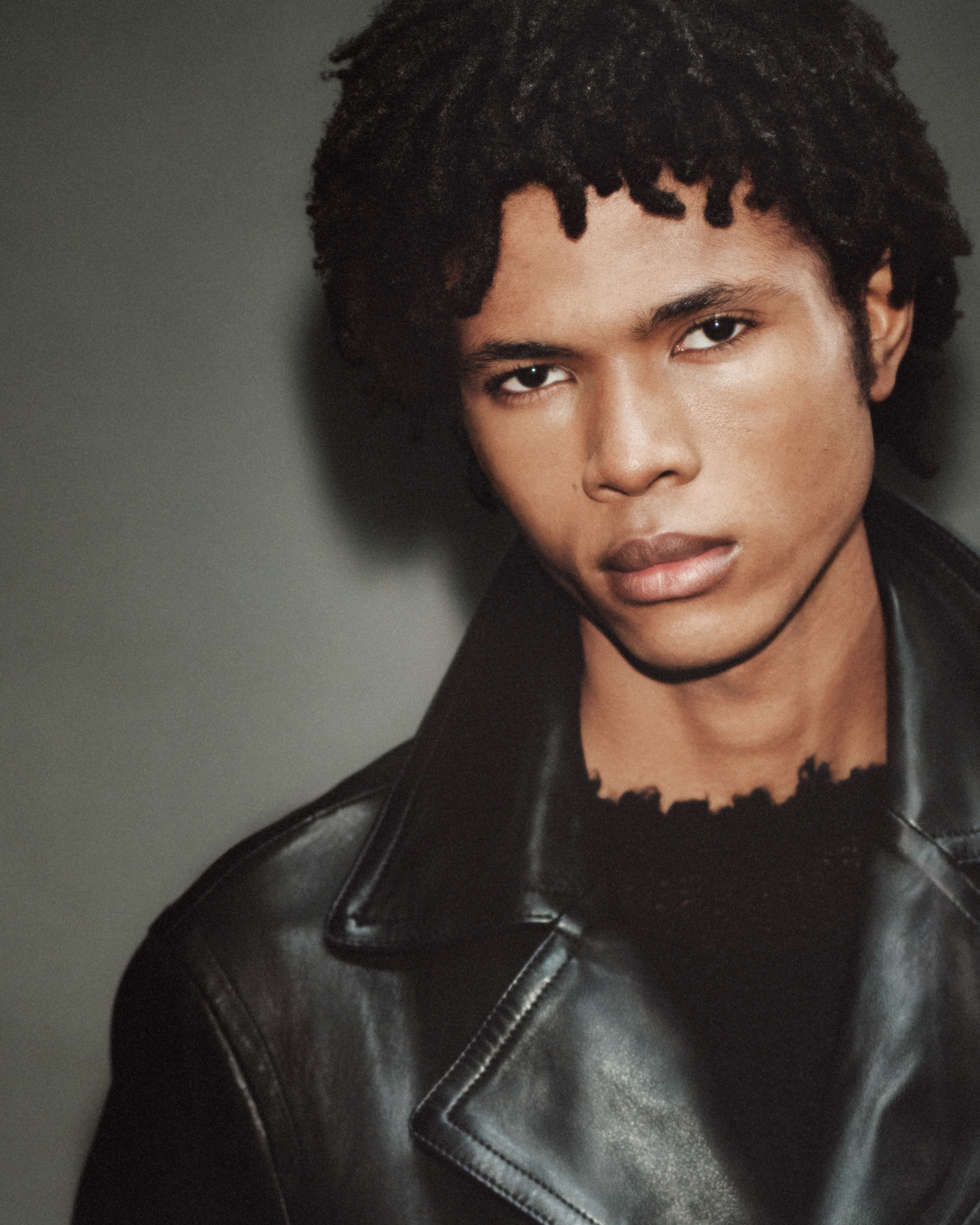Closeup of a male model wearing a frayed black jumper underneath a black leather jacket.