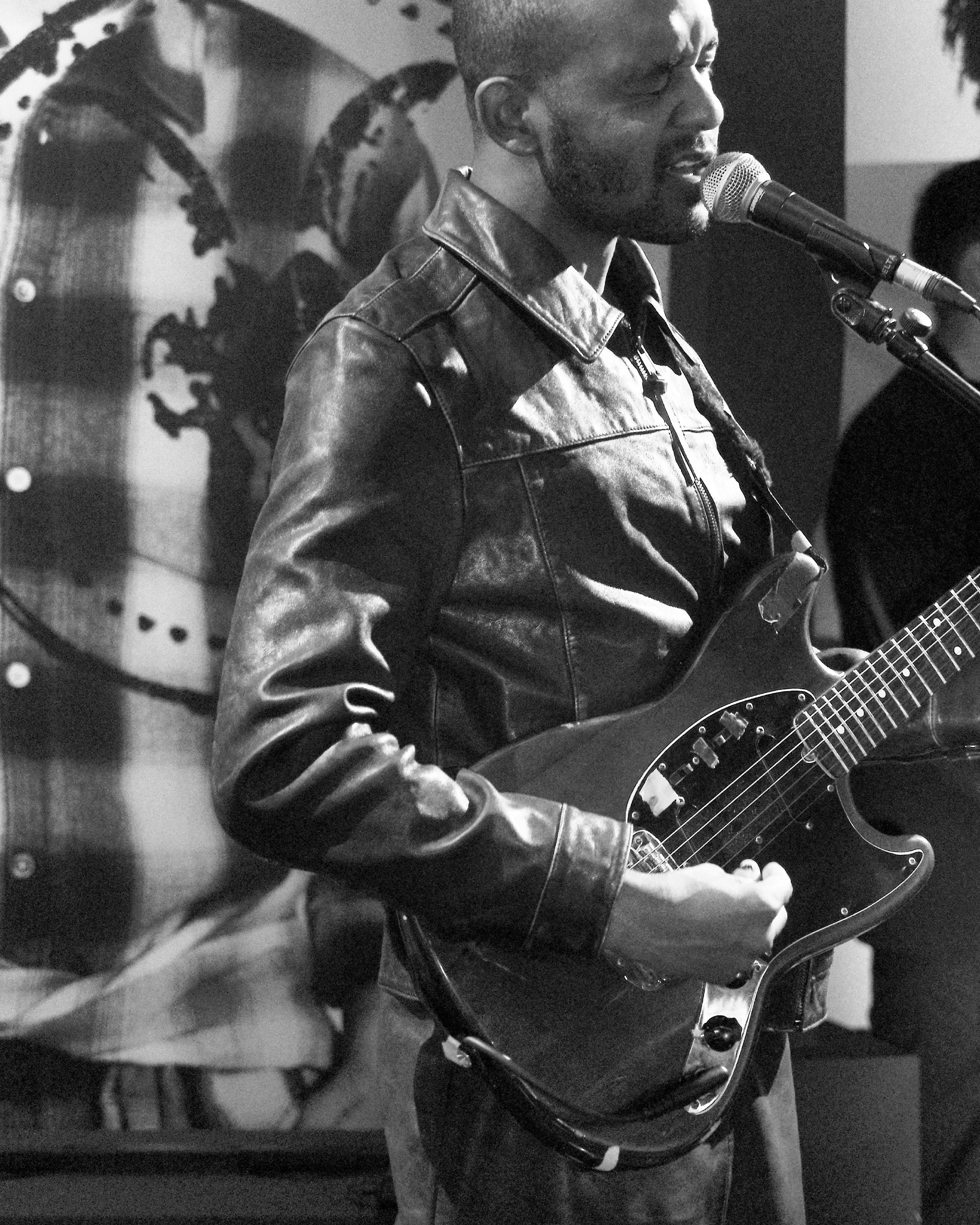 Black-and-white photo of a musician playing electric guitar and singing at the AllSaints Autumn Winter 26 Launch Party.