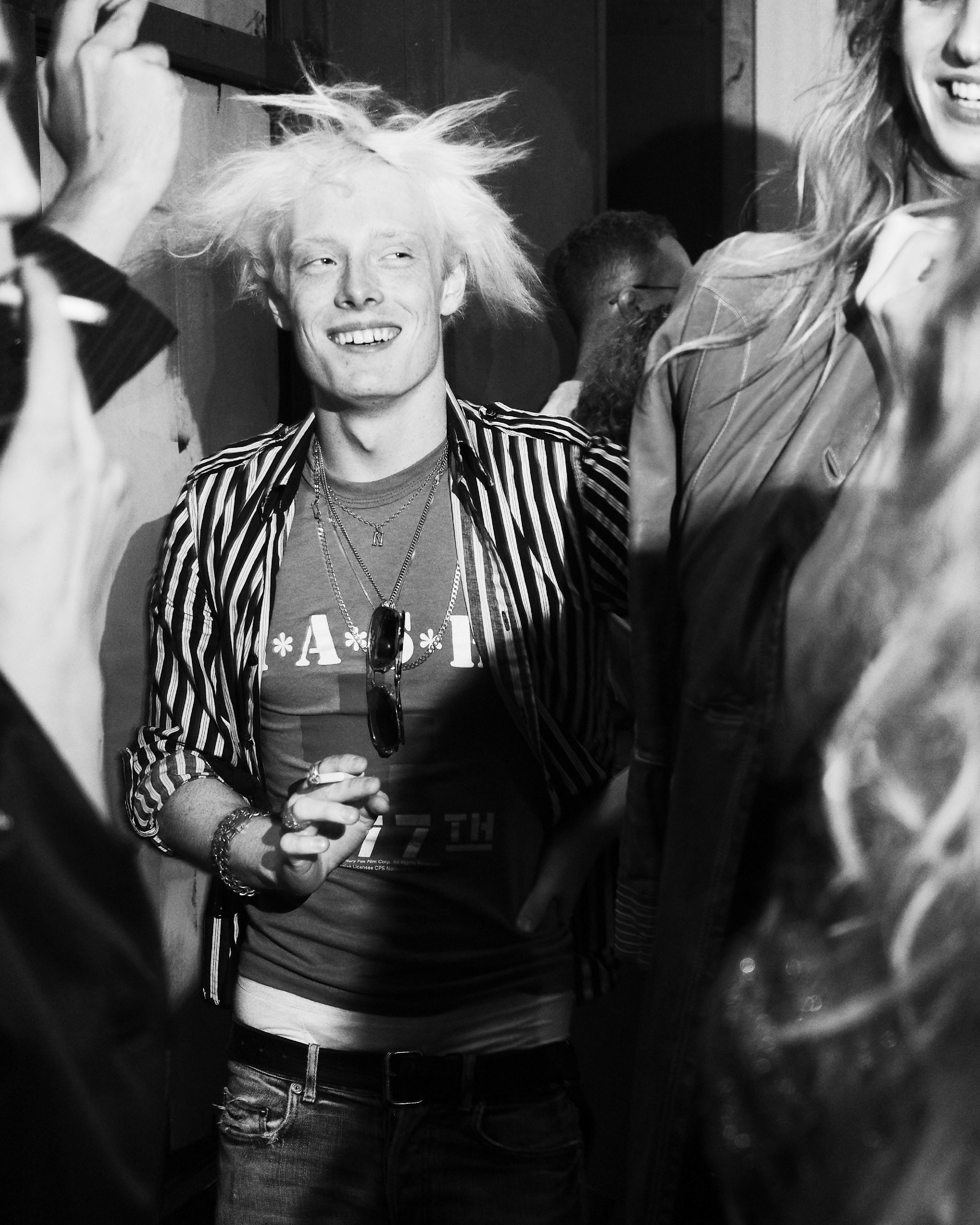Black-and-white photo of a smiling guest in a striped jacket at the AllSaints Autumn Winter 26 Launch Party.