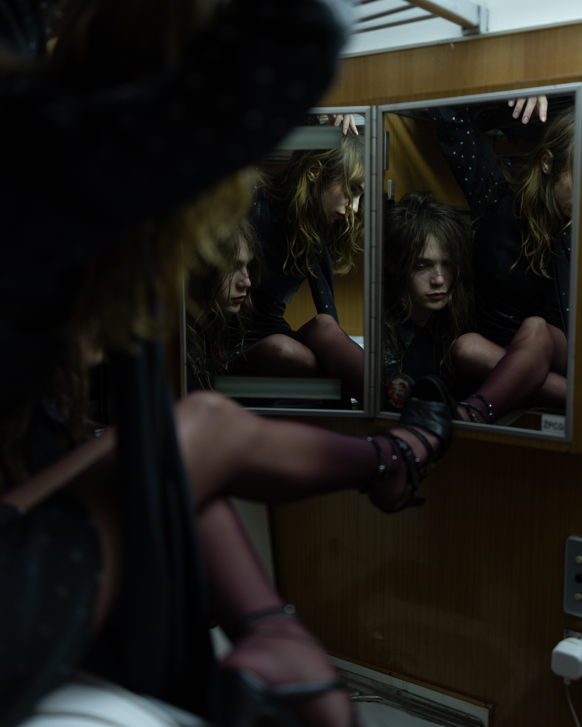 Portrait of a person seated inside a train compartment, reflected multiple times in mirrors beside the window.