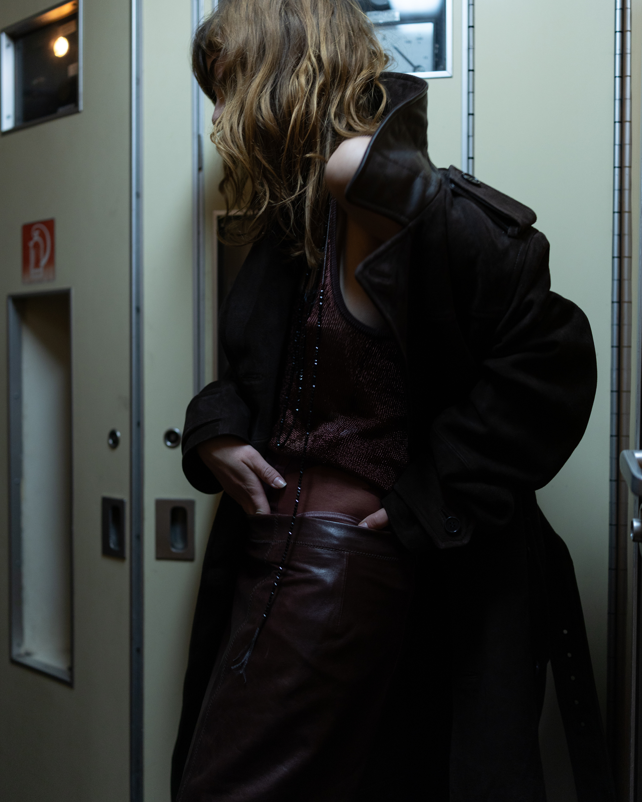 Portrait of a person wearing a dark oversized jacket and brown leather trousers inside a train carriage.